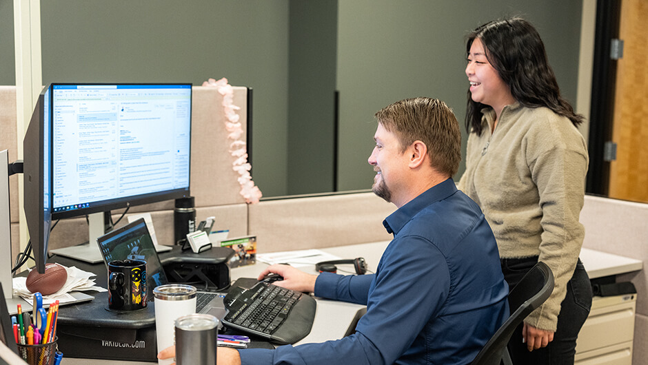 Two engineers working through a project on a computer screen in a cubicle.