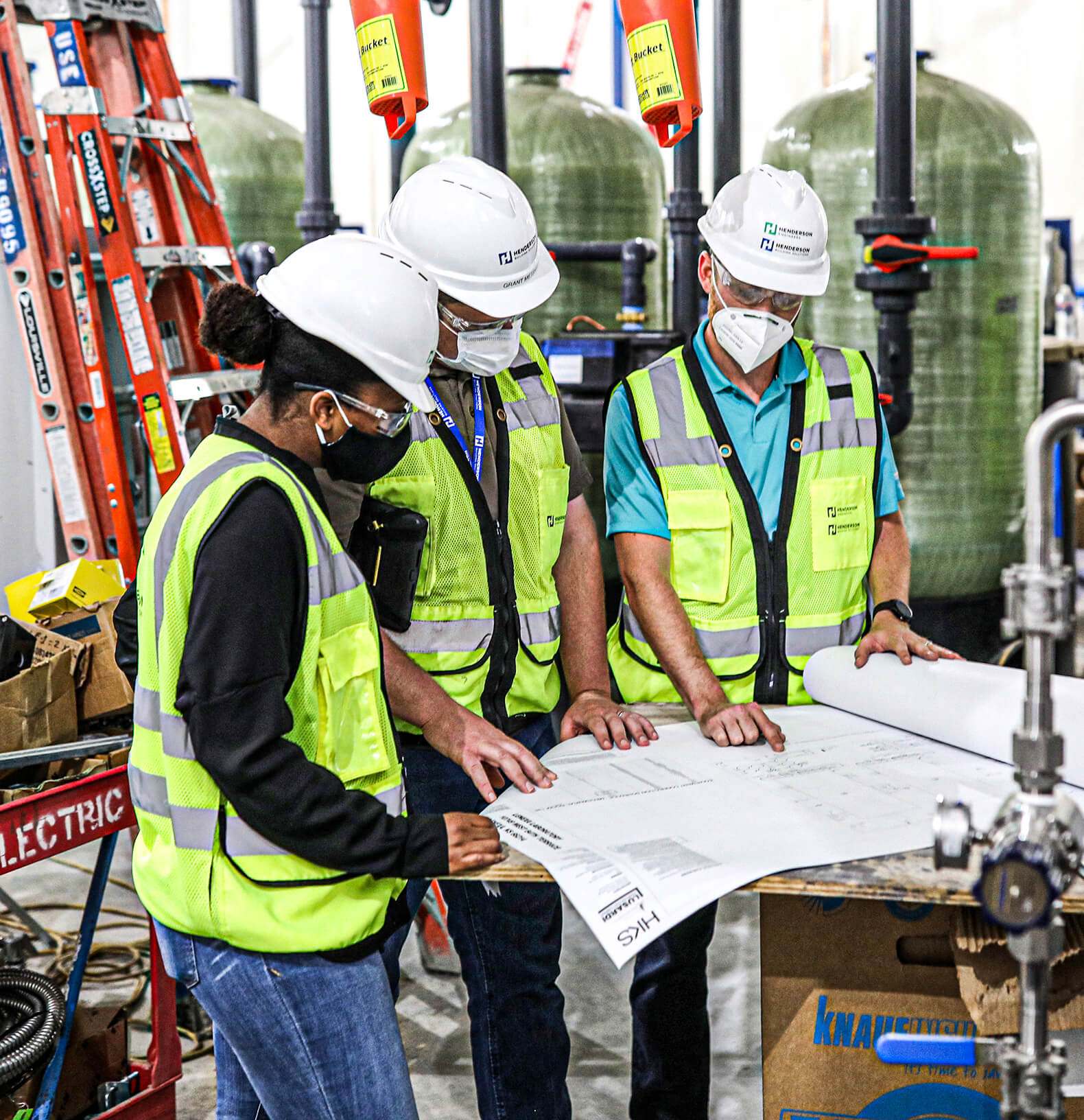 Three members of the Henderson Engineers leadership team chatting at a conference room table.