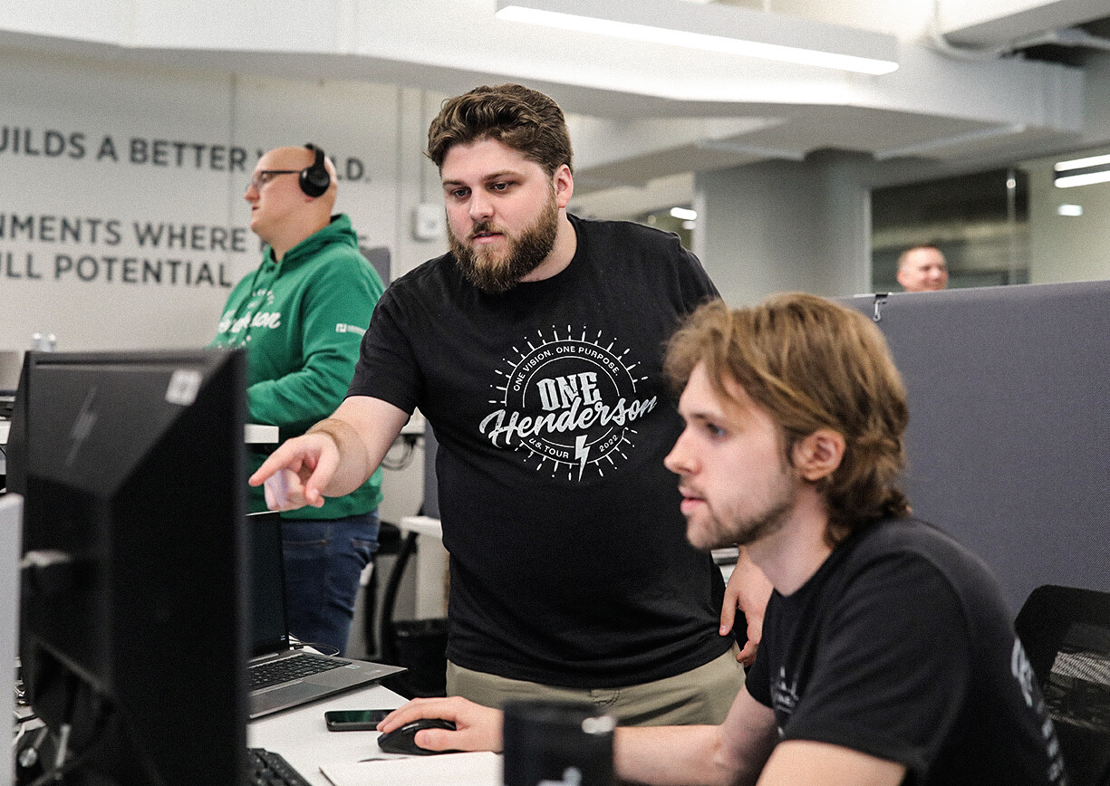 An engineer standing and pointing to a computer screen with another engineer seated.