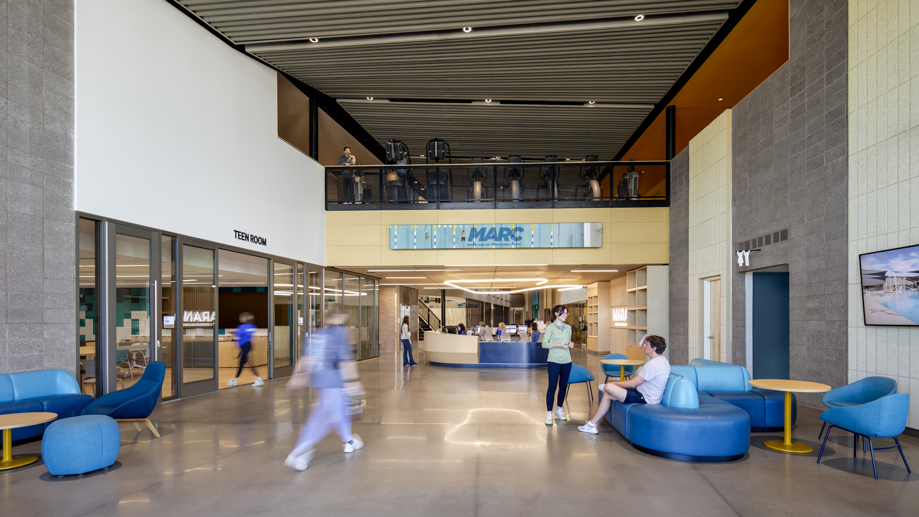 People walking and sitting around in the interior of a recreation center lobby.